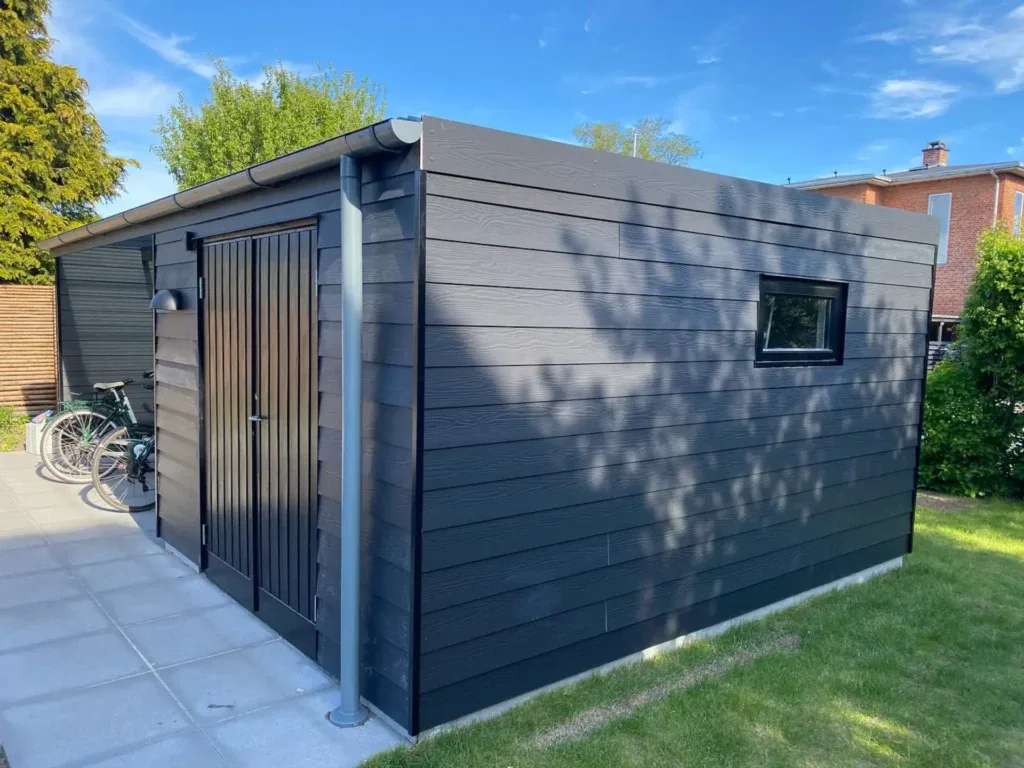 Moderne træhus med sort facade, lille vindue og udendørs område.