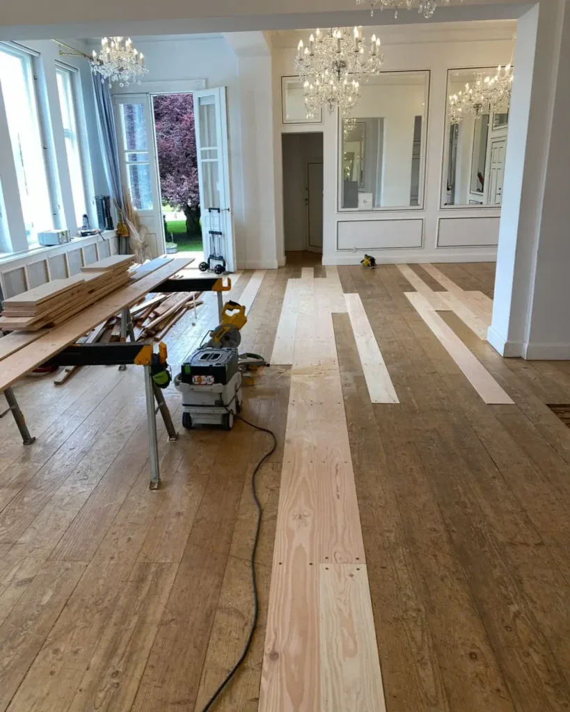 Renoveret stue med nyt trægulv og store vinduer, klar til færdiggørelse.