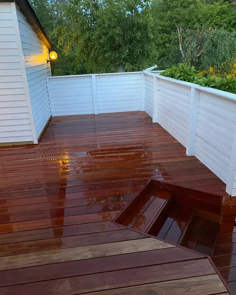 Nybehandlet trædæk med hvidt hegn og grønne omgivelser.