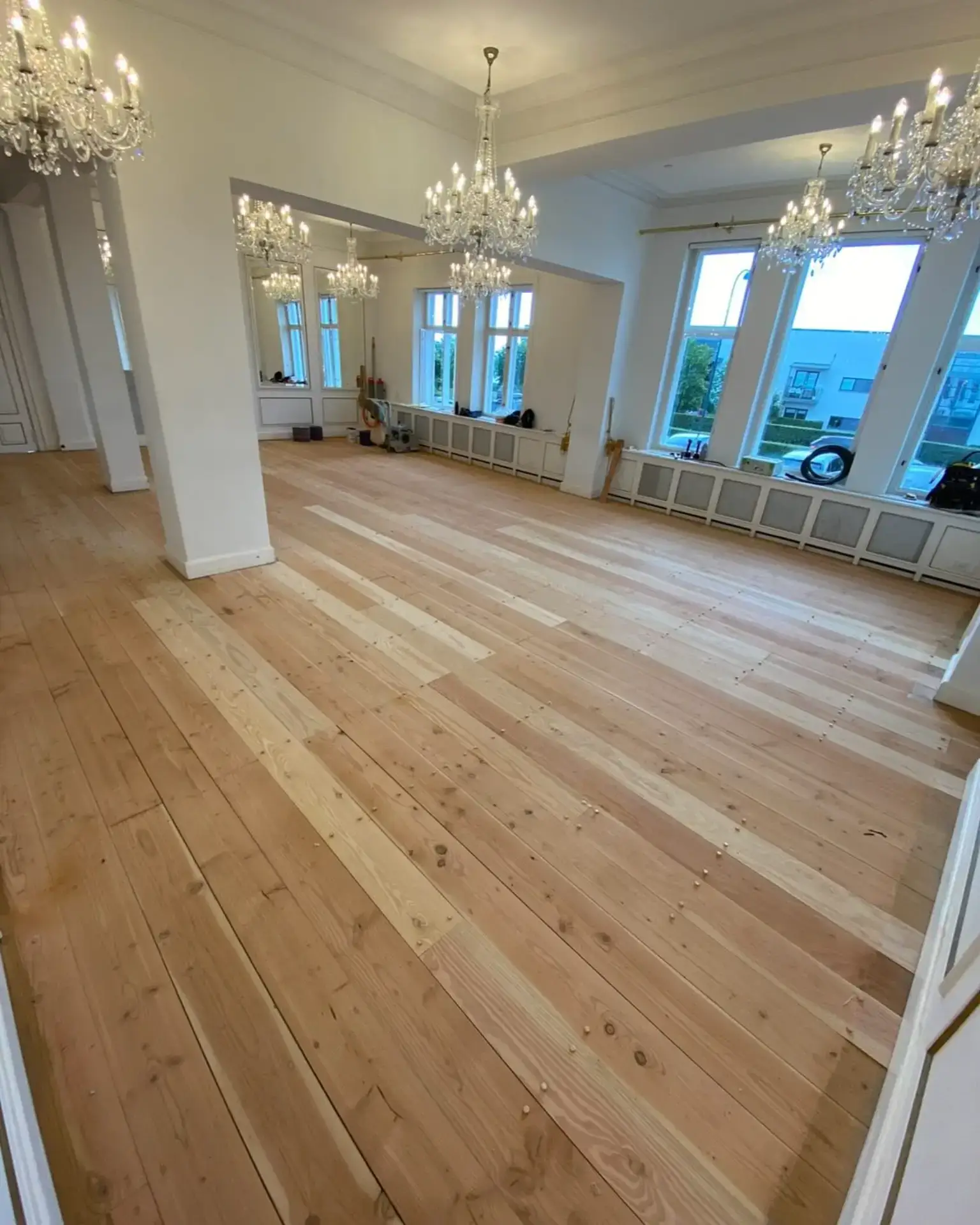 Elegant salon med trægulv og lyse vægge, store vinduer og lysekroner.