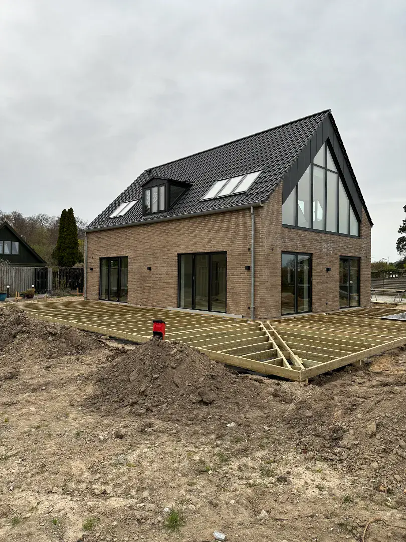 Nybygget moderne hus med store vinduer og skråtag under opførelse.