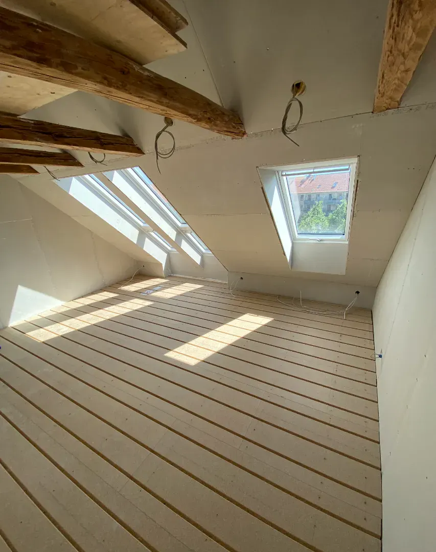 Udsigt over et nybygget loft med træbjælker og store tagvinduer.