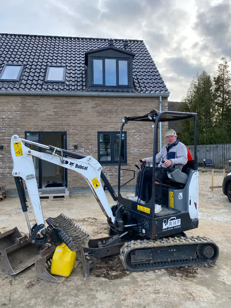 Minilæsser på byggeplads foran et nyt hus under opførelse.